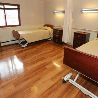 A clean, simple hospital room with two beds and wooden flooring.