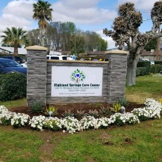 Outdoor sign for a healthcare facility surrounded by flowers and greenery.