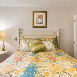 A cozy bedroom featuring a colorful bedspread, decorative pillows, and a lamp on a side table.