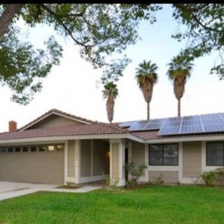 A suburban house with solar panels on the roof and a well-maintained lawn.