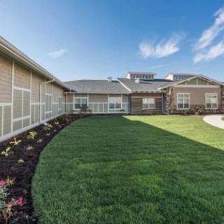 A well-manicured lawn and landscaped garden surround a modern building under a bright blue sky.