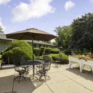 A sunny patio with outdoor seating, including a table and umbrella surrounded by lush greenery.