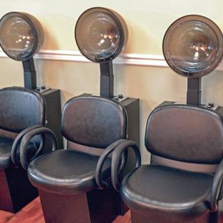 Three salon hair drying stations with chairs lined up against a wall.
