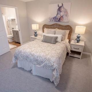 A cozy bedroom with a neatly made bed, flanked by two bedside tables with lamps, and adorned with a piece of horse artwork above the headboard.