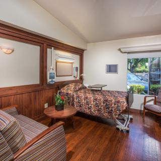 A well-furnished hospital room with a patient bed, seating area, and large window.