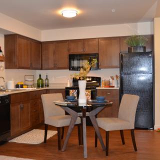 A modern kitchen with a small dining area featuring wooden cabinets, sleek appliances, and contemporary furniture.