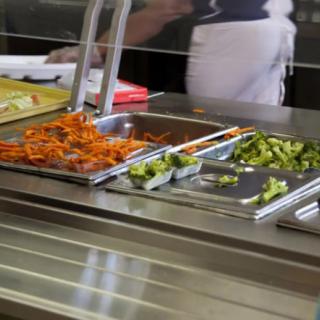 A cafeteria serving station with trays of food including vegetables.