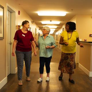 Three women engage in conversation while walking down a hallway.