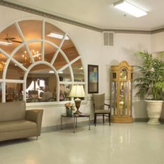 A cozy waiting area with a sofa, chairs, a lamp, and a grandfather clock by large arched windows.
