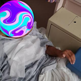 A patient rests in a hospital bed wearing a gown.