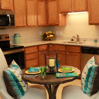 A cozy kitchen with a small dining area featuring wooden cabinets, modern appliances, and a table set for two.