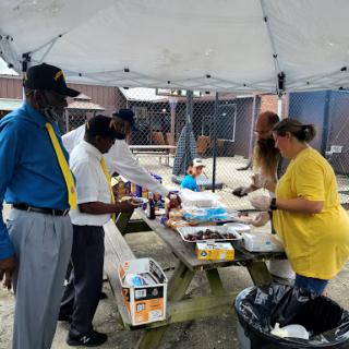 A group of people participating in a community food distribution event under a tent.