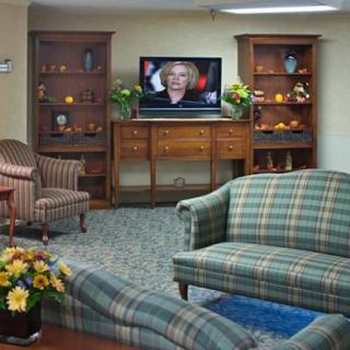 A cozy living room with classic decor featuring a sofa, armchairs, and a television surrounded by wooden shelves adorned with flowers.