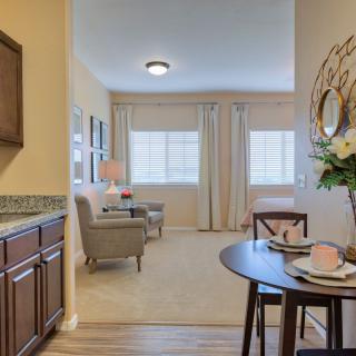 A cozy living space featuring a dining table set, elegant chairs, and large windows allowing natural light to flood the room.