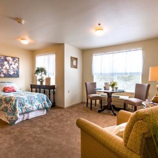 A cozy bedroom with a bed, seating area, and large window.