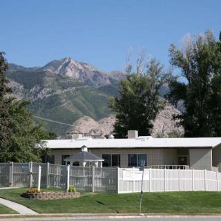 A single-story house with a white fence, set against a mountainous backdrop on a clear day.