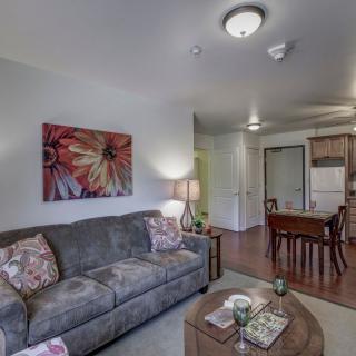 A cozy living room with a sofa, decorative pillows, artwork on the wall, and a view of the dining area.
