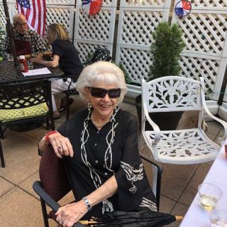 A woman in sunglasses sitting on a patio with an American flag in the background.