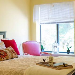 A cozy bedroom with a neatly made bed, decorative pillows, and a tray on the bed near a large window letting in natural light.