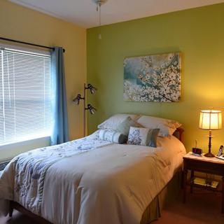 A cozy bedroom with a neatly made bed, soft lighting from a lamp, and wall art above the headboard.