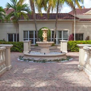 A scenic courtyard featuring a central fountain surrounded by palm trees and elegant landscaping.