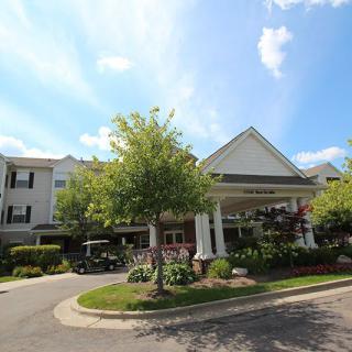 A well-maintained building entrance with lush landscaping and a clear blue sky.