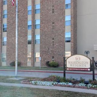 A residential building with a flagpole and landscaped flower beds.