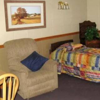 A cozy bedroom with a quilt-covered bed, a comfortable armchair, and a framed painting on the wall.