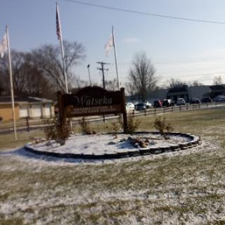 A welcoming sign surrounded by snow and grass, marking a local landmark on a winter day.
