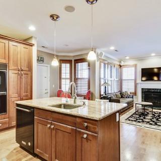A modern open-concept kitchen and living area featuring an island with wood cabinets, pendant lights, and a cozy fireplace.