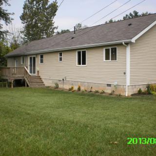 A single-story house with a wooden deck and a large backyard lawn.