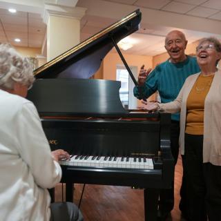 Elderly group enjoys singing together around a piano indoors.