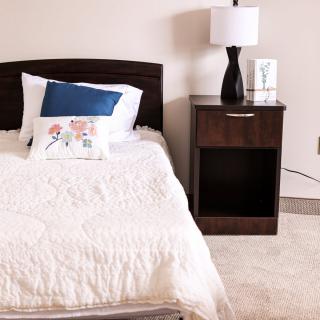 A cozy bedroom with a single bed, nightstand, and lamp.