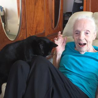 An elderly person joyfully interacting with a black cat while sitting comfortably at home.