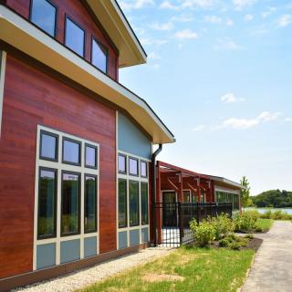 A modern building with large windows and wood paneling, set against a natural outdoor backdrop under a clear sky.