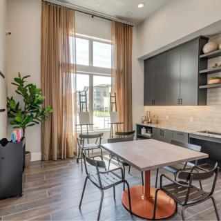 A modern dining area with natural light streaming through a large window, featuring a table surrounded by chairs, stylish shelving, and an indoor plant for added decor.