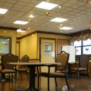 An empty dining room with arranged tables and chairs, illuminated by ceiling lights.