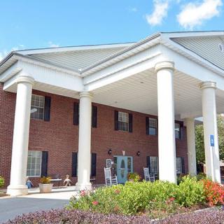 The image features a building with large white columns and a brick exterior, set against a clear blue sky.