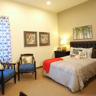 A cozy bedroom with a neatly made bed, two chairs, and stylish decor.