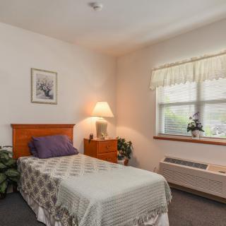 A simple and cozy bedroom with a single bed, dresser, and window.