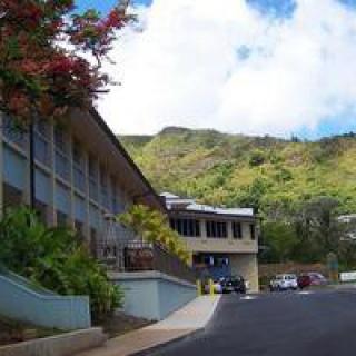 A building surrounded by lush greenery and mountains under a clear blue sky.