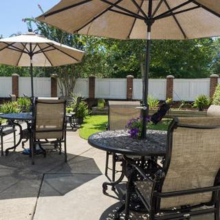 A sunny outdoor patio with tables, chairs, and umbrellas in a garden setting.