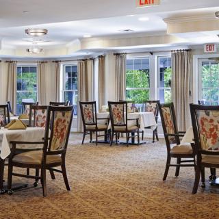A well-lit dining area with neatly arranged tables and floral upholstered chairs.