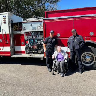 A heartwarming moment as firefighters pose with a community member in a wheelchair beside their fire truck.