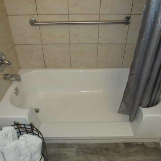 A clean bathtub with a shower curtain and towel basket in a tiled bathroom.