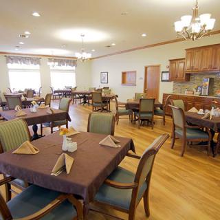 A spacious dining room with neatly arranged tables and chairs, featuring elegant chandeliers and a warm wooden floor.