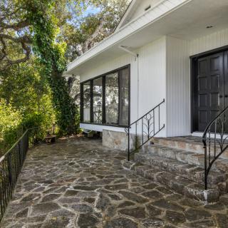 A view of a house with a stone patio and large windows surrounded by trees.