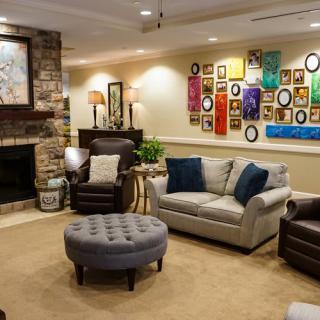 A cozy living room featuring a sofa and armchairs, complemented by an ottoman, fireplace, wall art, and decorative accents.