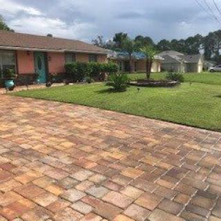 A suburban house with a spacious driveway made of pavers and a well-maintained lawn.