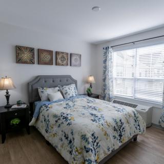 A well-decorated bedroom with floral bedding and ample natural light from a large window.